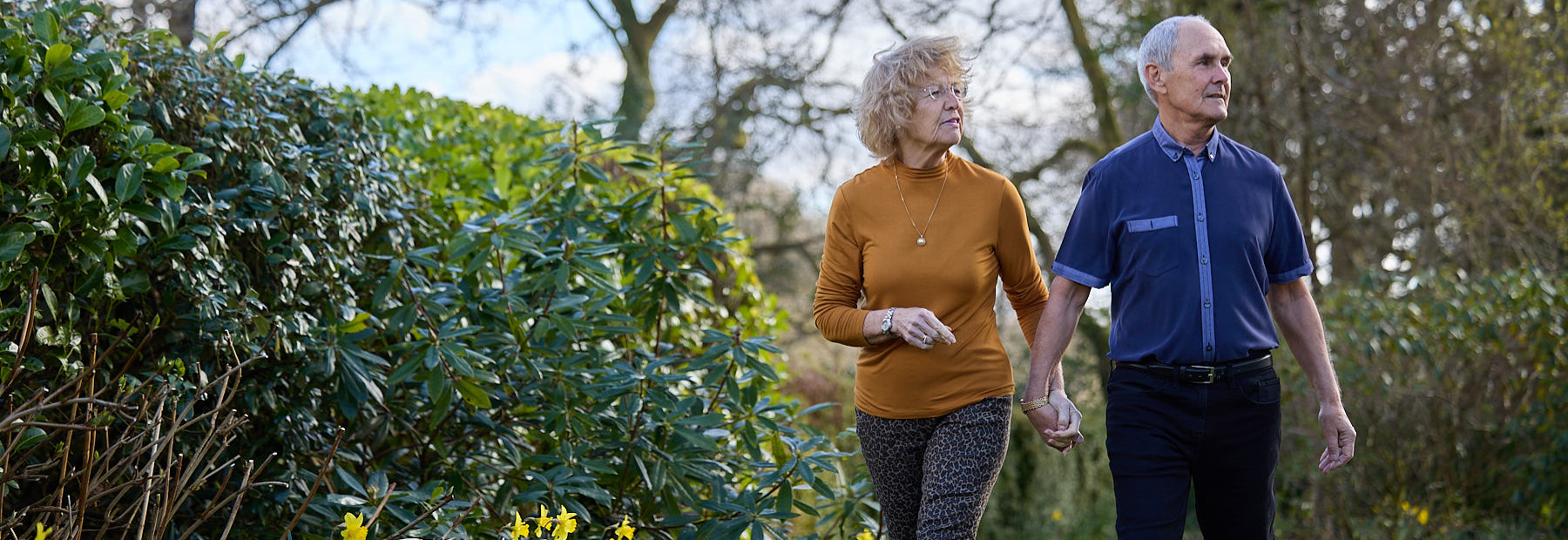 Member holding her partners hand walking through a garden