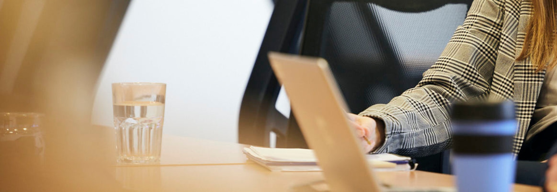 Laptop on desk zoomed in, person's hand writing in notebook